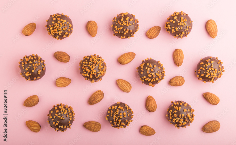 Chocolate caramel ball candies with almonds in a row on a pastel pink background. top view. Chocolate caramel ball candies with almonds in a row on a pastel pink background. top view.