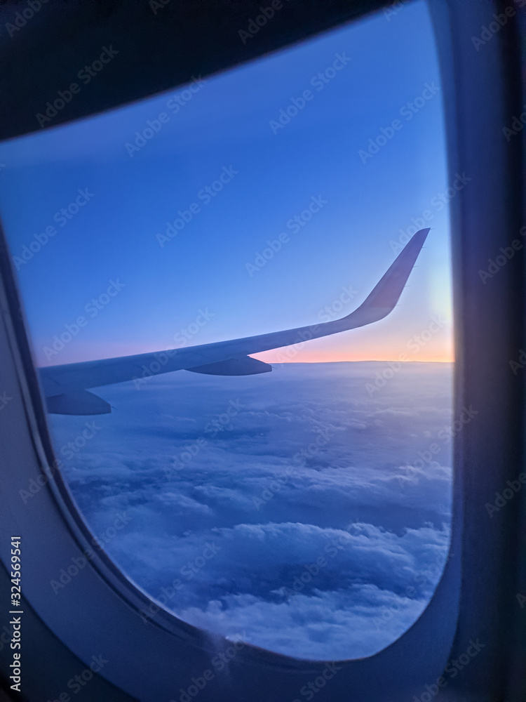 Beautiful view through the open window in airplane on the wing and clouds at sunrise litght