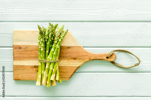 Cooking asparagus. Bunch steams on cutting board on green wooden background top-down