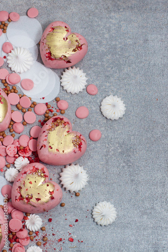 Pink hearts from tempered chocolate with chocolate drops, meringues and dried berries on grey background photo