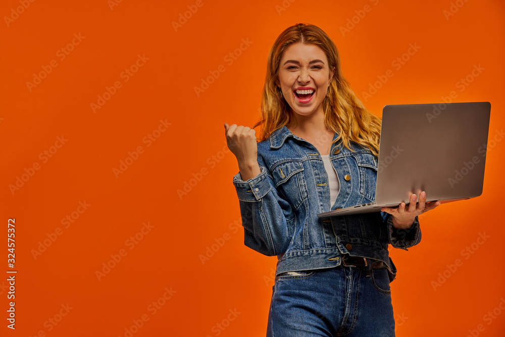 Happy woman in a jeans/denim jacket with fair wavy hair with laptop shows victory gesture. Happy woman in a jeans/denim jacket with fair wavy hair with laptop shows victory gesture.
