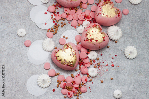 Pink hearts from tempered chocolate with chocolate drops, meringues and dried berries on grey background