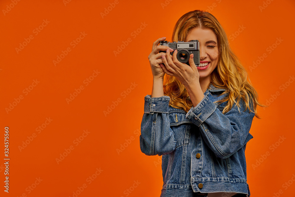 Smiling woman in a jeans jacket with fair wavy hair takes a photo on old photo camera. Smiling woman in a jeans jacket with fair wavy hair takes a photo on old photo camera.