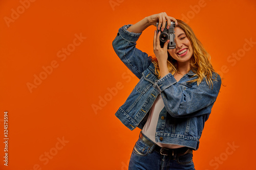 Smiling woman in a jeans jacket with fair wavy hair takes a photo on old photo camera.