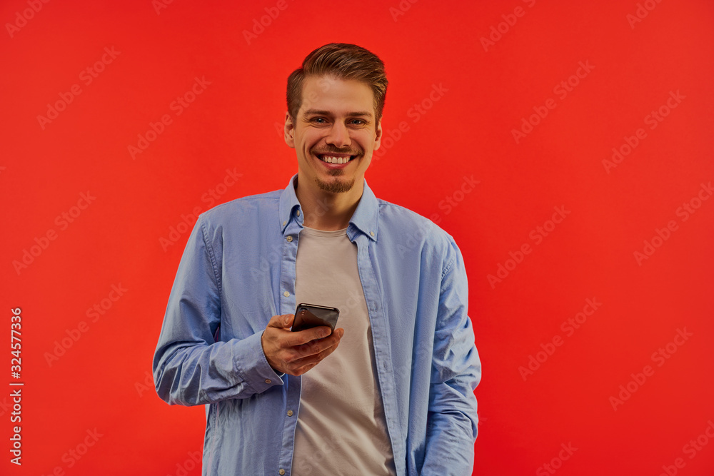 Happy man with a beard in a blue shirt holds phone.