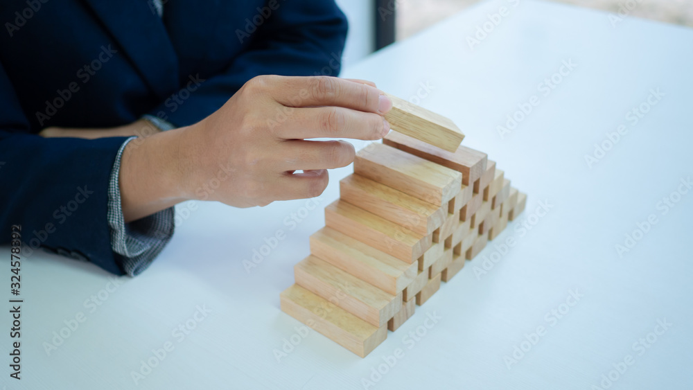 Businessman hand is placing the wooden pieces. Pyramid shape. Business development concept