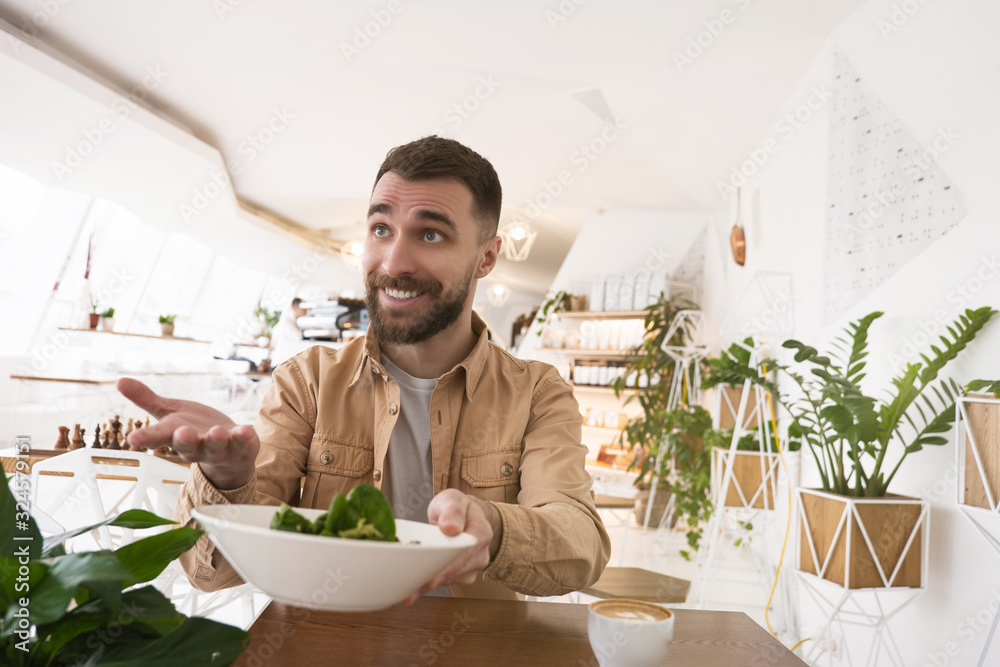 young smiling man holds plate with salad having lunch at cafe during break young smiling man holds plate with salad having lunch at cafe during break