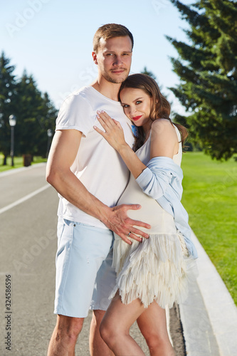 Happy couple in love waiting for child pregnancy hug walk in the summer park green trees nature husband and wife baby boy young family parent, man woman romantic dating harmony relationship.