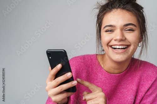 Image of excited beautiful woman pointing finger at cellphone