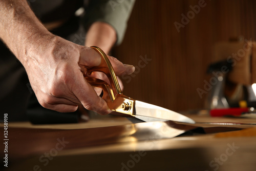 Man cutting leather with scissors in workshop, closeup