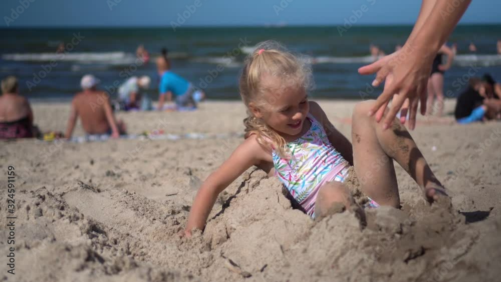 girl buried in sand break free and have fun with mother. Blurred people and sea girl buried in sand break free and have fun with mother. Blurred people and sea