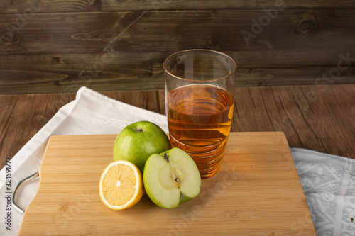 A glass of lemon apple juice with fruits around on a wooden board