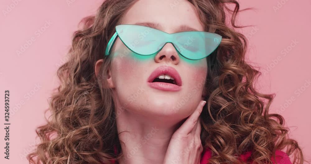 Sensually Girl showing her Emotions to the Camera. Sexually Woman posing it trendy Sunglasses on Studio. Having modern Makeup and curly Hairstyle. Beautiful Girls. Fashion. Sexy Young Woman.
