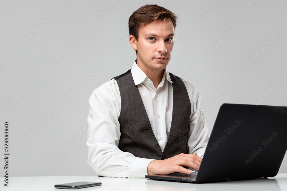 Businessman in a white t-shirt and grey vest working on a laptop. Man looking at the camera Businessman in a white t-shirt and grey vest working on a laptop. Man looking at the camera