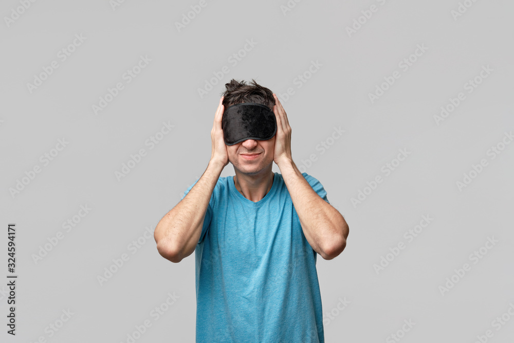 Sleepy man with black sleep mask on a head screaming closing ears isolated over grey background Sleepy man with black sleep mask on a head screaming closing ears isolated over grey background