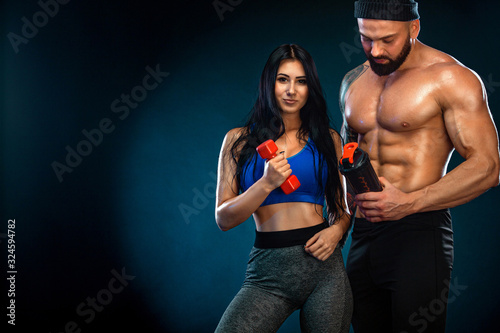 Athletic couple. Man and fit woman with sports equipment on dark background. photo