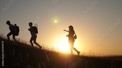 children and mom with backpacks travel climb mountain in sun. mom and daughters go camping. Family of tourists with kids traveling at sunset. joint work of tourists. movement to victory.