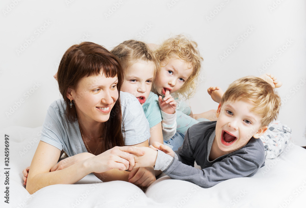 Family time: Mom and three children lie on a white bed, hugging and laughing cheerfully. Family time: Mom and three children lie on a white bed, hugging and laughing cheerfully.
