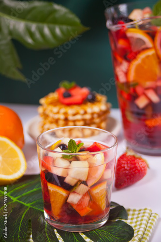 Red wine fresh sangria or punch with fruits, mint leaves and berries. Homemade waffles on the background.