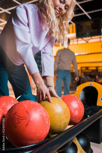 smiling blonde girl choosing bowling ball in bowling club