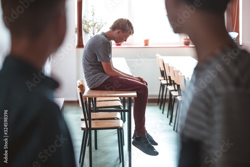Sad teenage boy sitting alone at school, bullying among children concept photo