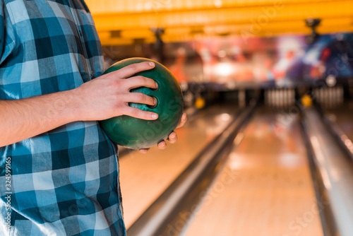 cropped view of young man holding bowling ball near skittle alley