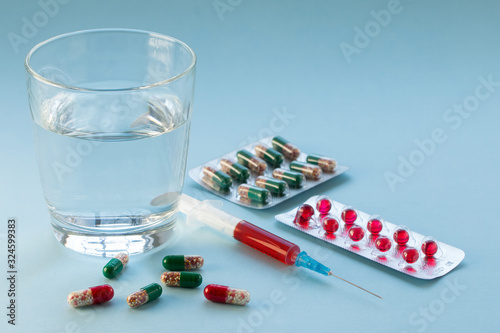 Tablets in blister pack, syringe with vaccine and glass of water on blue background. photo