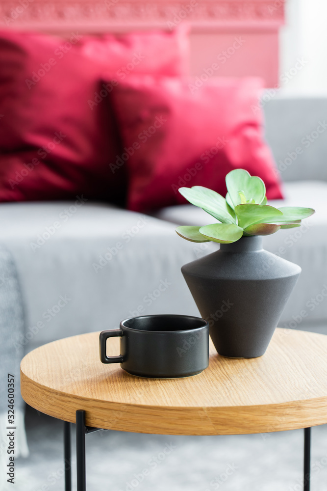 Green flowers in black vase next to black coffee cup on wooden coffee table in stylish interior