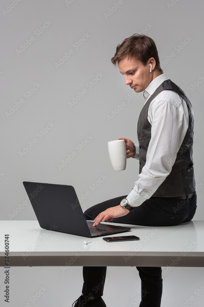 Man drinking coffee sitting on a white table with laptop and smartphone Man drinking coffee sitting on a white table with laptop and smartphone