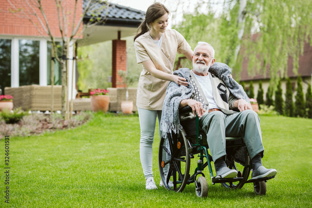 Senior man with helpful volunteer in the garden of professional care home Senior man with helpful volunteer in the garden of professional care home