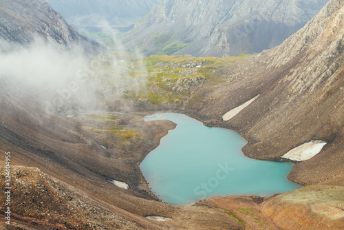 Atmospheric minimalist alpine landscape with beautiful glacial lake in highland valley among rocky mountains. Pieces of snow around mountain lake among stony rocky slope of glacier. Wonderful scenery.
