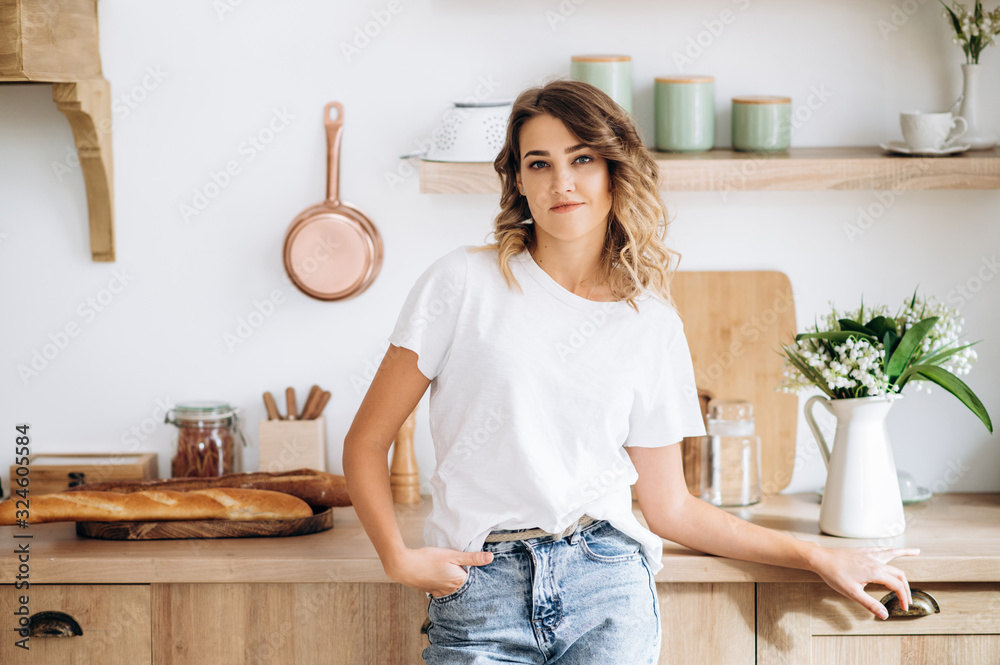 Beautiful blue-eyed blonde girl in a white T-shirt and jeans with an attractive smile posing in the kitchen Beautiful blue-eyed blonde girl in a white T-shirt and jeans with an attractive smile posing in the kitchen