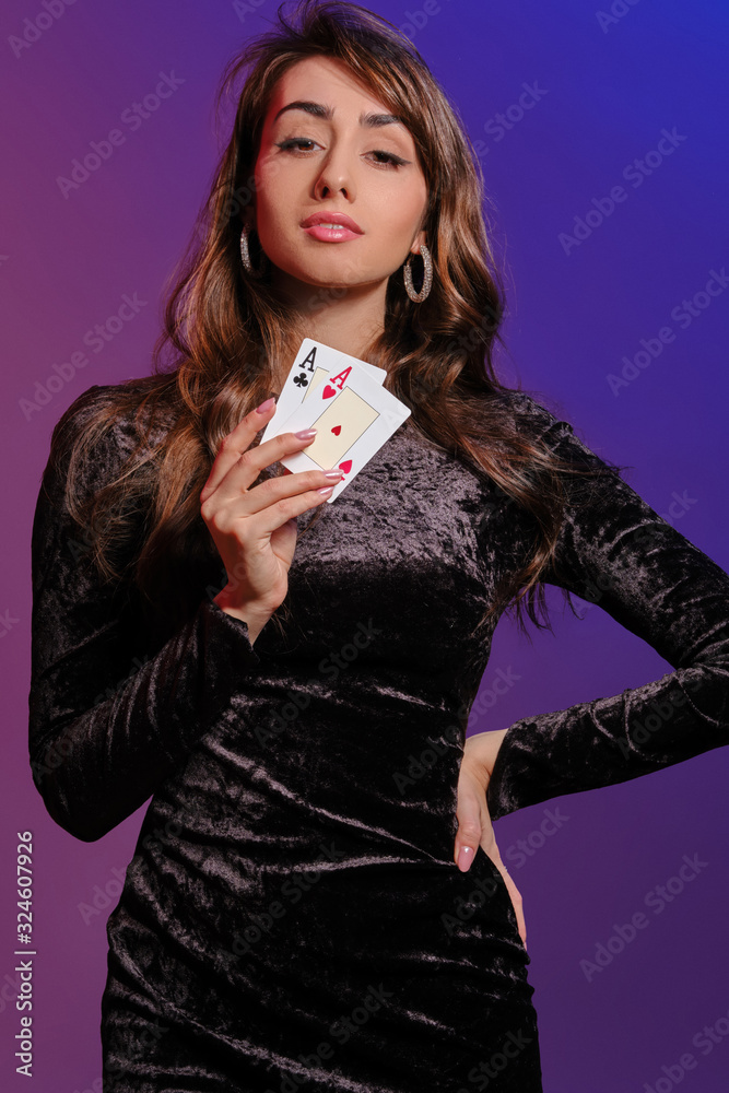 Brunette woman in black velvet dress showing two playing cards, posing against coloful background. Gambling entertainment, poker, casino. Close-up. Brunette woman in black velvet dress showing two playing cards, posing against coloful background. Gambling entertainment, poker, casino. Close-up.