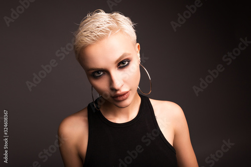 Beautiful short-haired blonde in a studio on a gray background. The girl with a suspicious look.