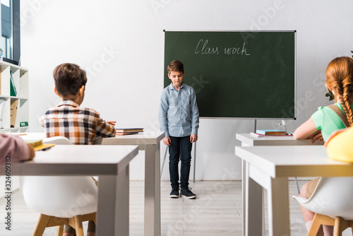 schoolkids sitting at desks near classmate near chalkboard with class work lettering