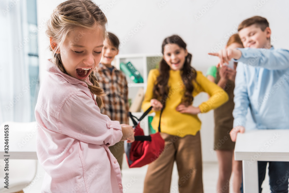 selective focus of bullied schoolgirl screaming near cruel cruel pupils holding backpack and pointing with fingers selective focus of bullied schoolgirl screaming near cruel cruel pupils holding backpack and pointing with fingers