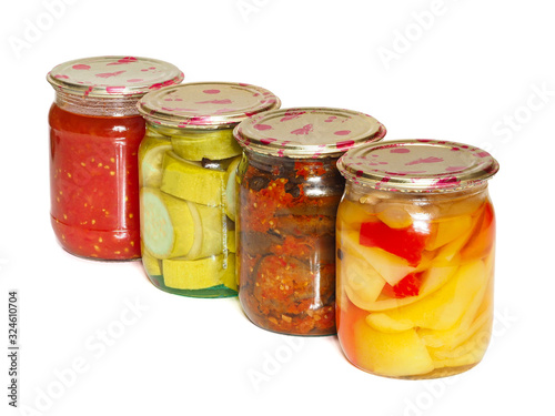 Jars of tasty pickled vegetables, bell peppers, eggplant, zucchini and tomato juice on a white background