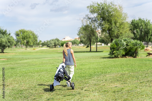 Blonde girl with sunglasses dragging a golf cart in the middle of a golf course