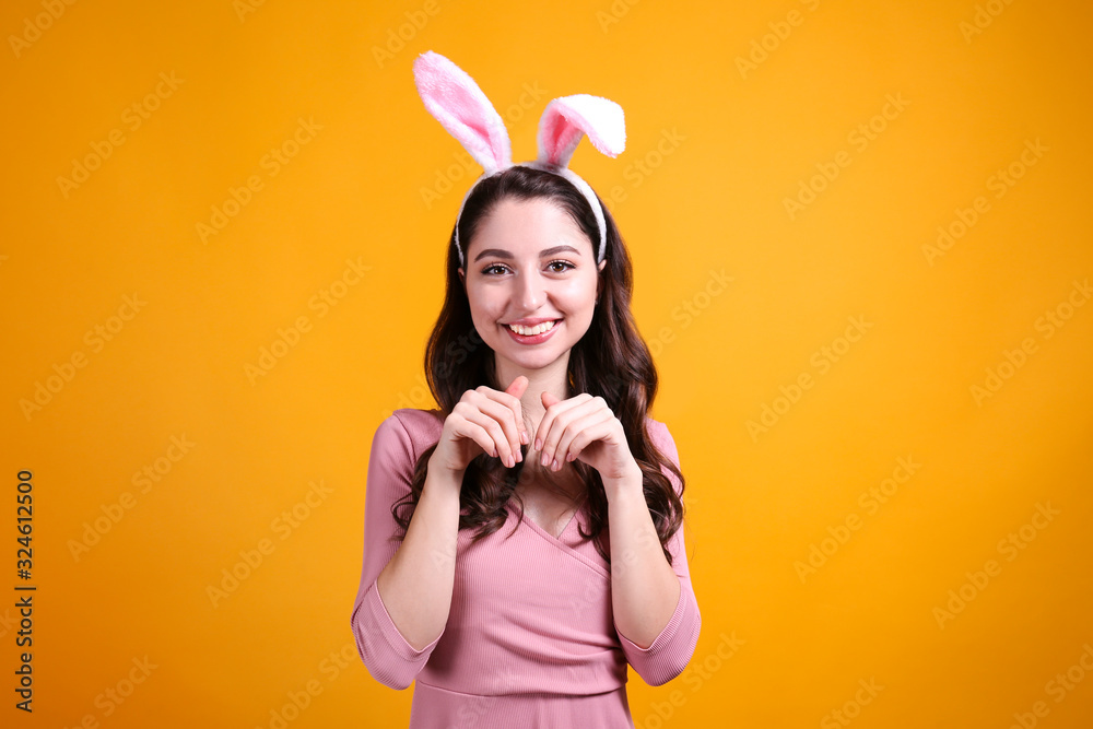 Studio portrait of young beautiful woman wearing traditional bunny ears headband for easter and smiling. Brunette female with wavy hair over yellow background. Close up, copy space. Studio portrait of young beautiful woman wearing traditional bunny ears headband for easter and smiling. Brunette female with wavy hair over yellow background. Close up, copy space.