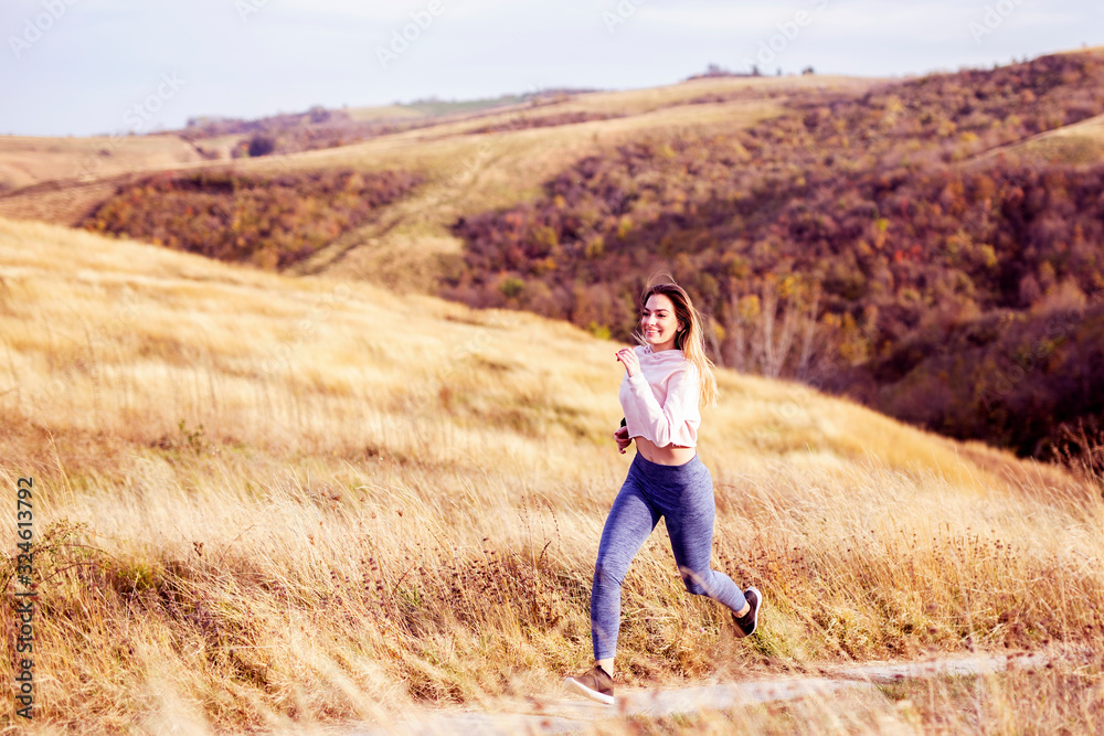 Woman in sportware running in the nature with dry grass and glade on background Woman in sportware running in the nature with dry grass and glade on background