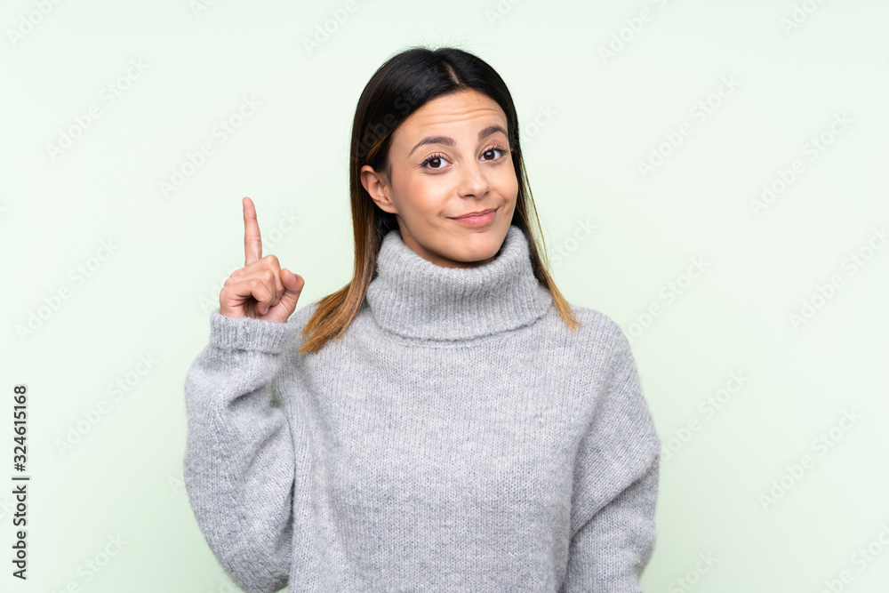 Woman wearing a sweater over isolated green background pointing with the index finger a great idea