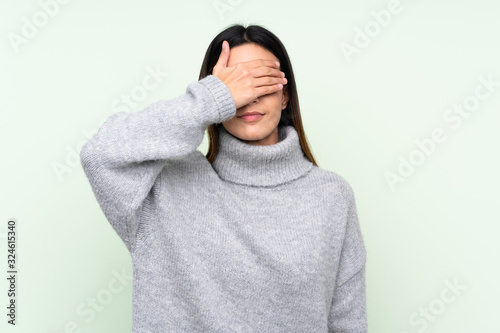 Woman wearing a sweater over isolated green background covering eyes by hands © luismolinero