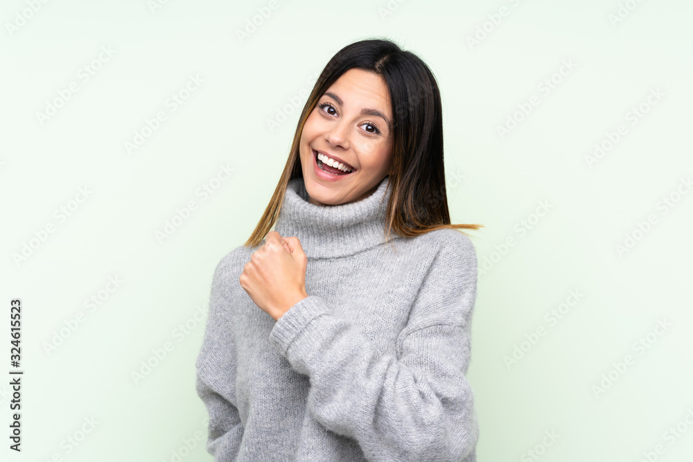 Woman wearing a sweater over isolated green background celebrating a victory Woman wearing a sweater over isolated green background celebrating a victory