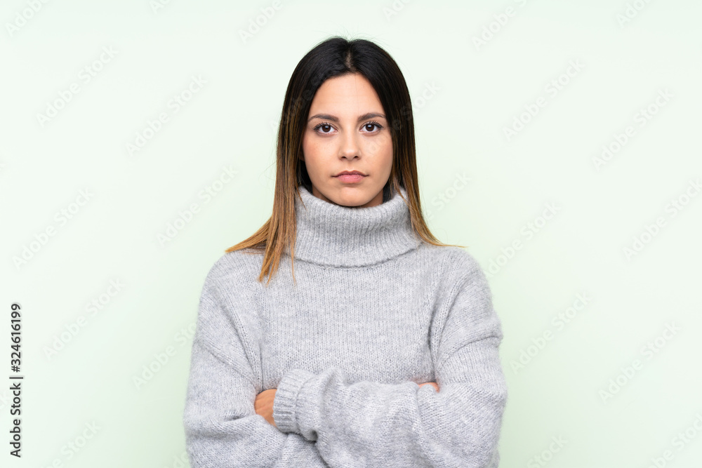 Woman wearing a sweater over isolated green background keeping arms crossed