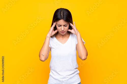 Young woman over isolated yellow background with headache
