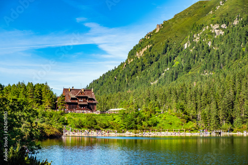 Panoramic view of the Morskie Oko mountain lake surrounding larch, pine and spruce forest with Schronisko przy Morskim Oku shelter house in background