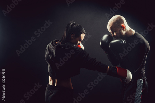 Woman exercising with trainer at boxing and self defense lesson, studio, smoke on background. © zamuruev