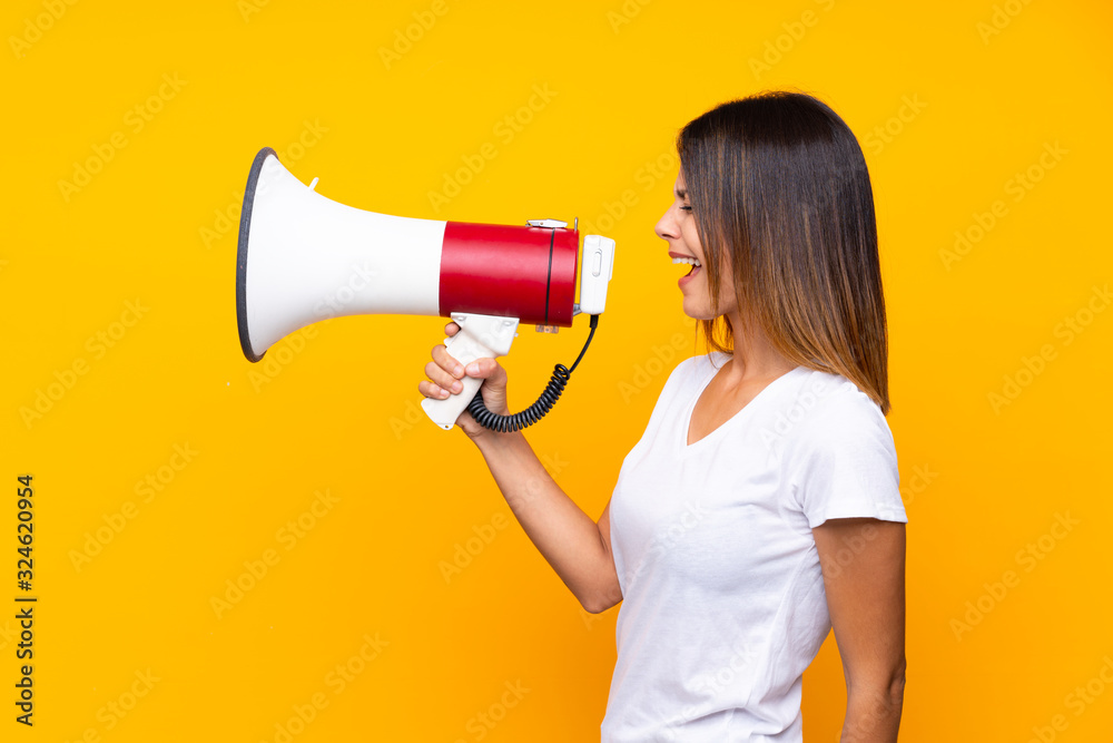 Young woman over isolated yellow background shouting through a megaphone Young woman over isolated yellow background shouting through a megaphone