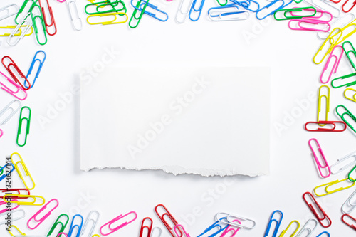 Colorful paper clips and torned paper frame in the centre of composition isolated on white.