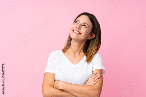 Young woman over isolated pink background looking up while smiling photo